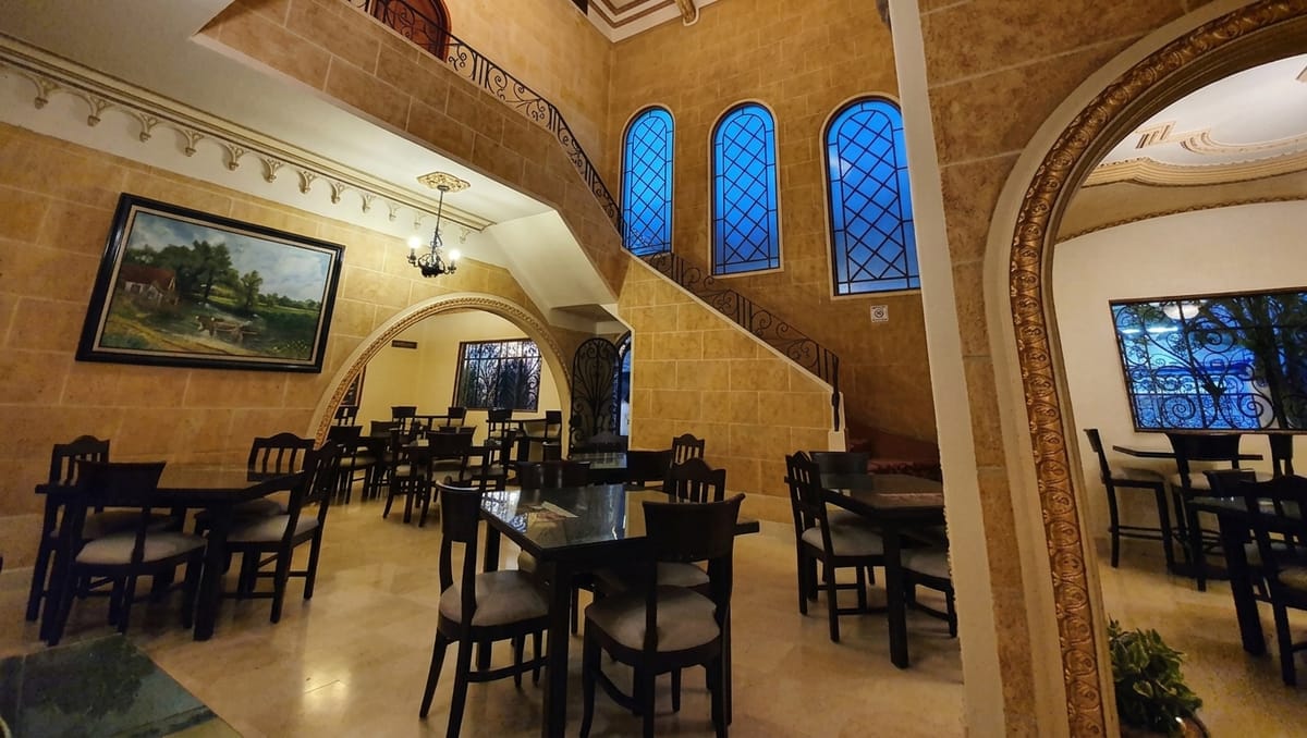 Comedor de Bennoni con arcos de cantera, vitrales y mesas de madera