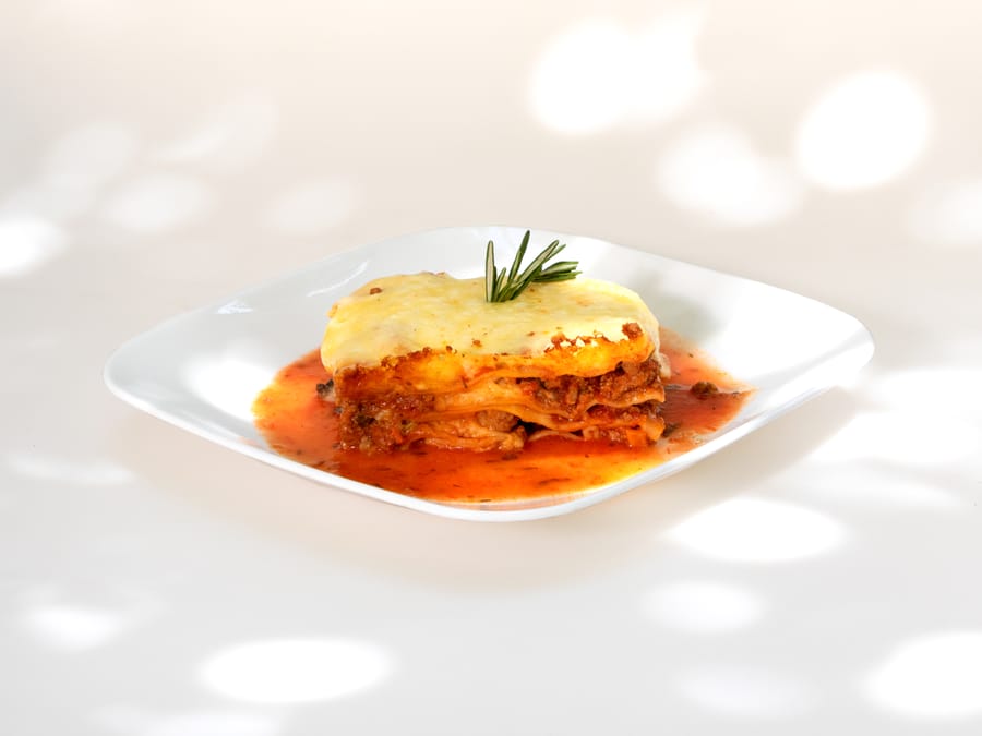 Porción de lasaña gratinada servida en plato blanco