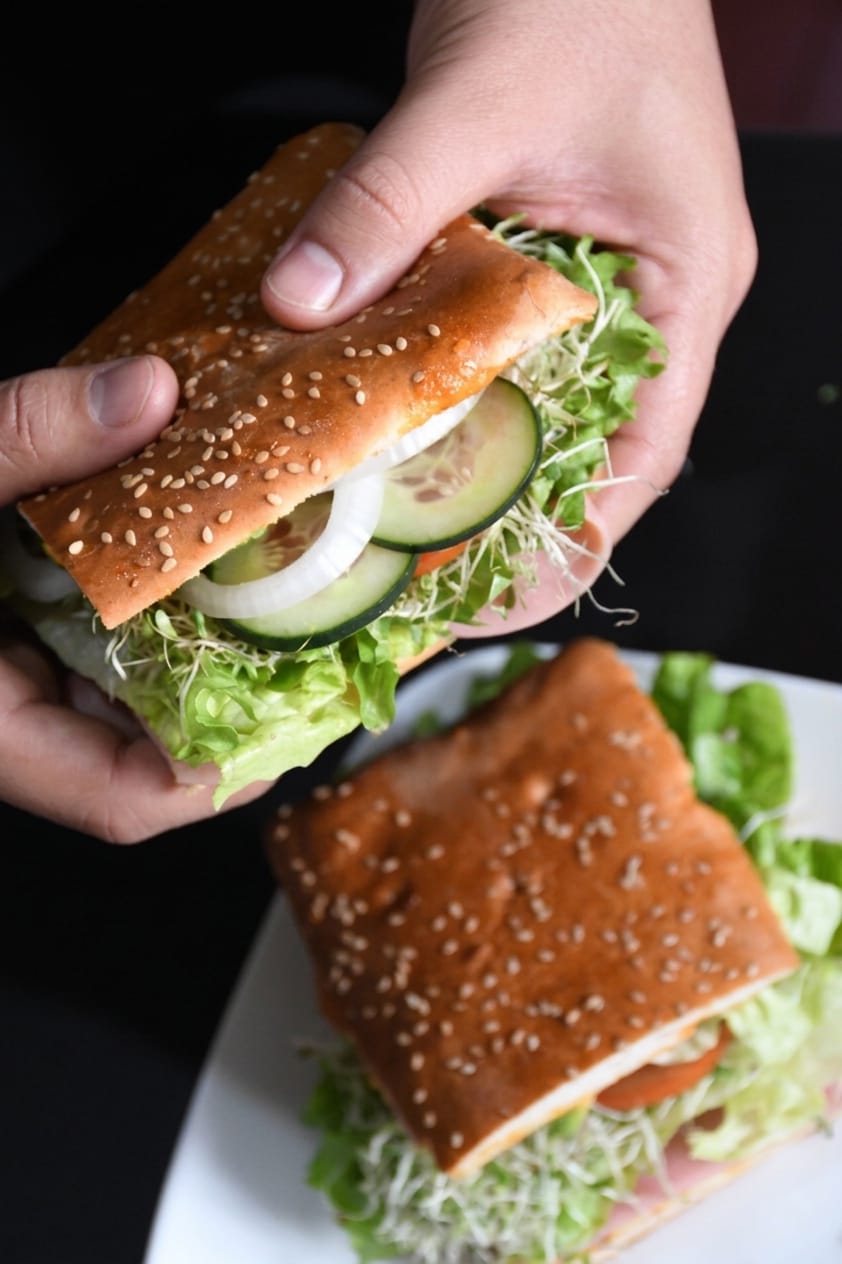 Manos sosteniendo una torta en pan de ajonjolí con lechuga y pepino
